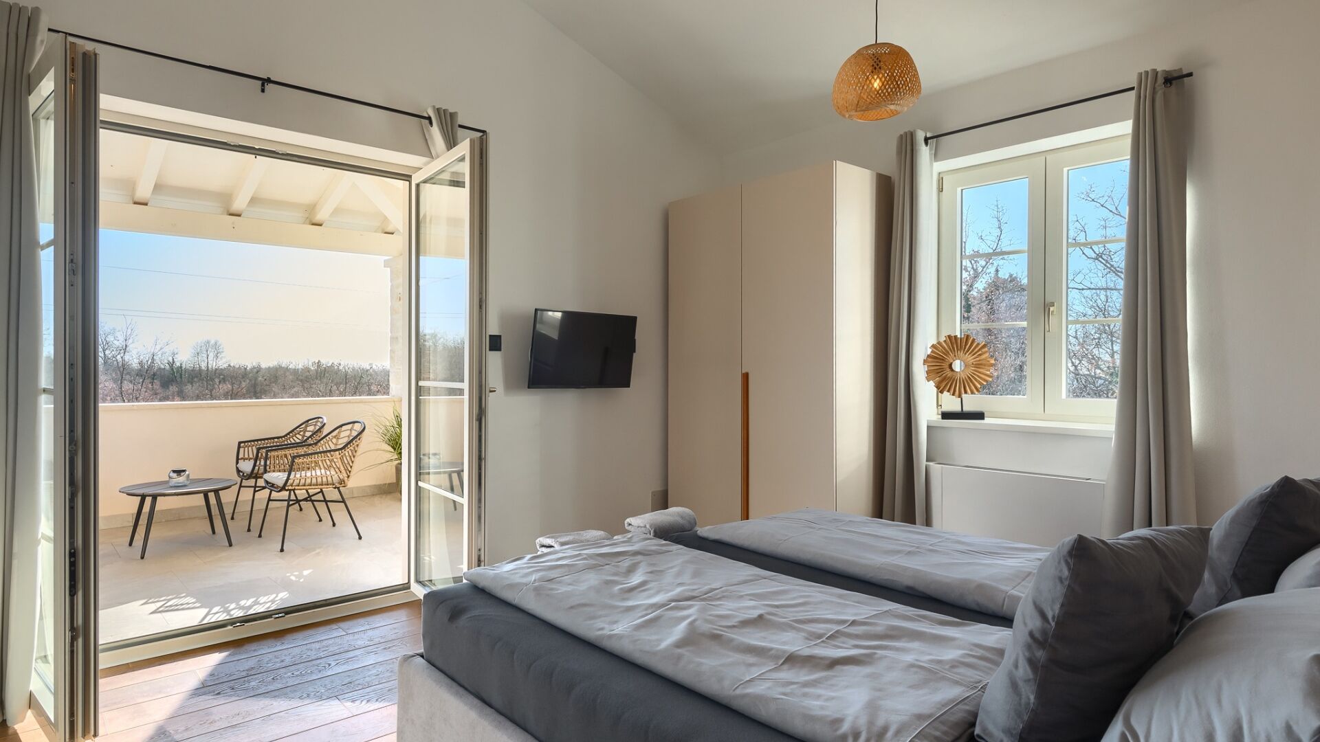 A bedroom with a bed, a TV, a balcony with chairs, and a window with curtains.