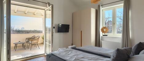 A bedroom with a bed, a TV, a balcony with chairs, and a window with curtains.