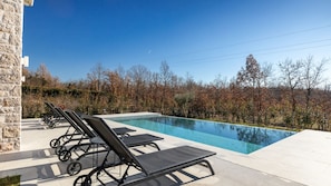 A swimming pool with lounge chairs, surrounded by trees and a stone wall. - Villa LeGro by Villas Guide (Rapavel)