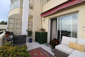 Un balcon avec un canapé blanc, une table à manger et des chaises. On y trouve également des plantes en pot et un tapis à motifs.