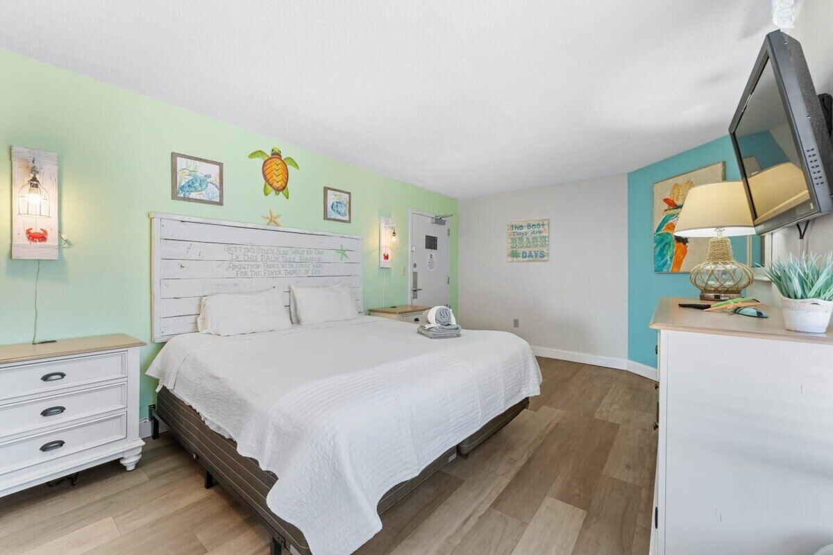 A bedroom with a bed, a nightstand, a dresser, a TV, and wall decorations.