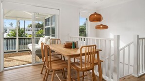 A dining area with a wooden table and chairs, a wicker pendant light, and a view of the outdoors through a sliding glass door. - Four bedroom  in Australia, Anna Bay (Anna Bay)