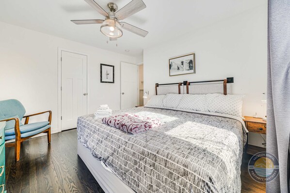 A bedroom with a bed, a ceiling fan, a chair, and a nightstand.