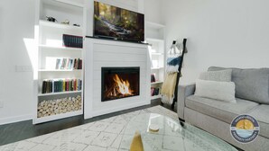 Ein modernes Wohnzimmer mit Kamin, einer Wand-TV und einem Bücherregal.