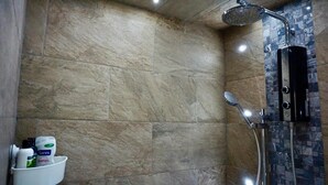 A bathroom with beige tiles, a shower with a handheld showerhead, and a soap dispenser. - Stunning 1-bed Apartment in Bishop Auckland (Bishop Auckland)