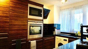 A modern kitchen with built-in appliances, including a microwave, oven, and washing machine, and a large window with sheer curtains. - Stunning 1-bed Apartment in Bishop Auckland (Bishop Auckland)