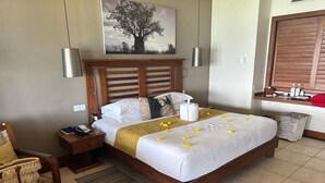 Una camera d'albergo con un letto di legno, un comodino con il telefono, una sedia con un asciugamano e un quadro appeso al muro.