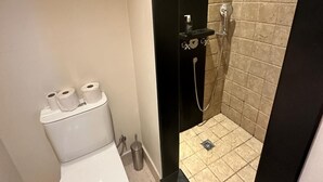 Un bagno con il water, uno spazio doccia e un portasciugamani per carta igienica.