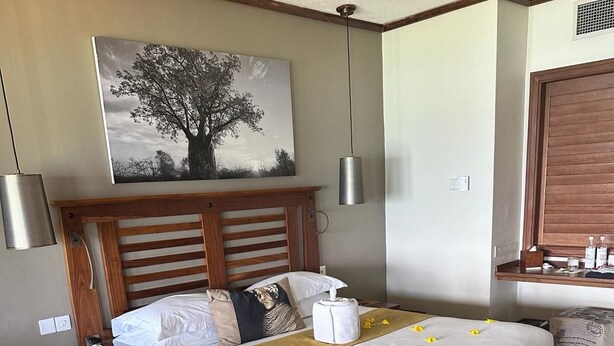 Una camera d'albergo ben ordinata con un letto grande, un comodino con il telefono, un tavolino con una sedia, un quadro appeso alla parete e una finestra con persiana in legno.