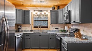 A modern kitchen with dark cabinets, stainless steel appliances, a granite countertop, and a central island with a sink. - Serene Cabin, Sleeps 6・Hot Tub・Pool Table & Arcade (Pigeon Forge)