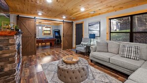 A cozy living room with a fireplace, a sofa, a coffee table, and a pool table. - Serene Cabin, Sleeps 6・Hot Tub・Pool Table & Arcade (Pigeon Forge)