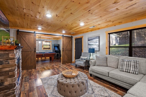 A cozy living room with a fireplace, a sofa, a coffee table, and a pool table.