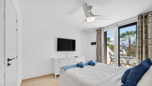 A bedroom with a bed, a TV, a ceiling fan, and a view of palm trees. - Parque Santiago II Exceptional Duplex with terrace (Costa Adeje)