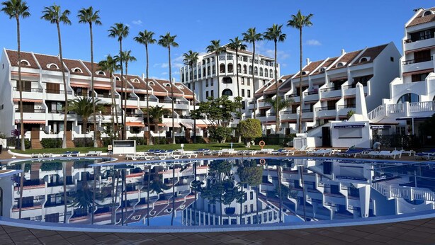 A resort with a central pool surrounded by lounge chairs, palm trees, and multi-story buildings with balconies. - Parque Santiago II Exceptional Duplex with terrace (Costa Adeje)