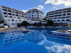 A hotel with a central pool, multiple balconies, and a clear sky.