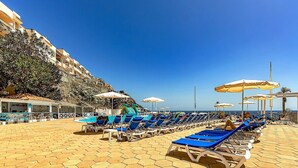 Un hôtel situé en bord de mer, doté d’un sol carrelé à motifs hexagonaux, de chaises longues, de parasols et offrant une vue sur la mer.