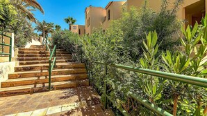Un escalier avec des rampes vertes menant à un bâtiment aux murs de couleur beige, sous un ciel d’un bleu clair.