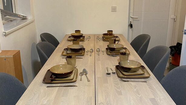 Une table à manger dressée avec des bols, des cuillères et un luminaire suspendu au-dessus.