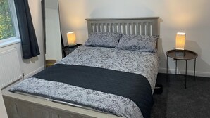 Une chambre à coucher avec un lit, deux lampes de chevet, une table de chevet et une fenêtre avec des rideaux.