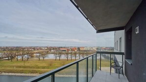 Ein Balkon mit Blick auf einen Fluss, Bäume und entfernte Gebäude.