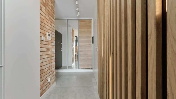 Ein Flur mit Backsteinwand, Schiebeglasdoor und Wandpaneelen aus Holz.