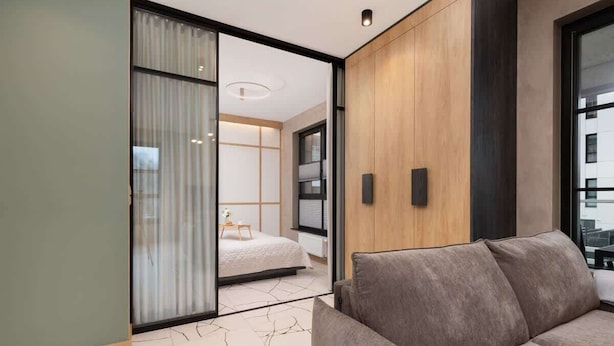 A modern room with a sofa, a bed, and a sliding door leading to another room.