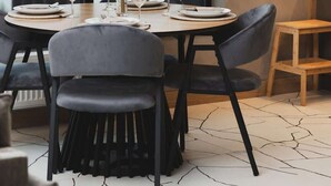 A dining area with a round table set for four, black chairs, a hanging light fixture, and a large window with a view of buildings.