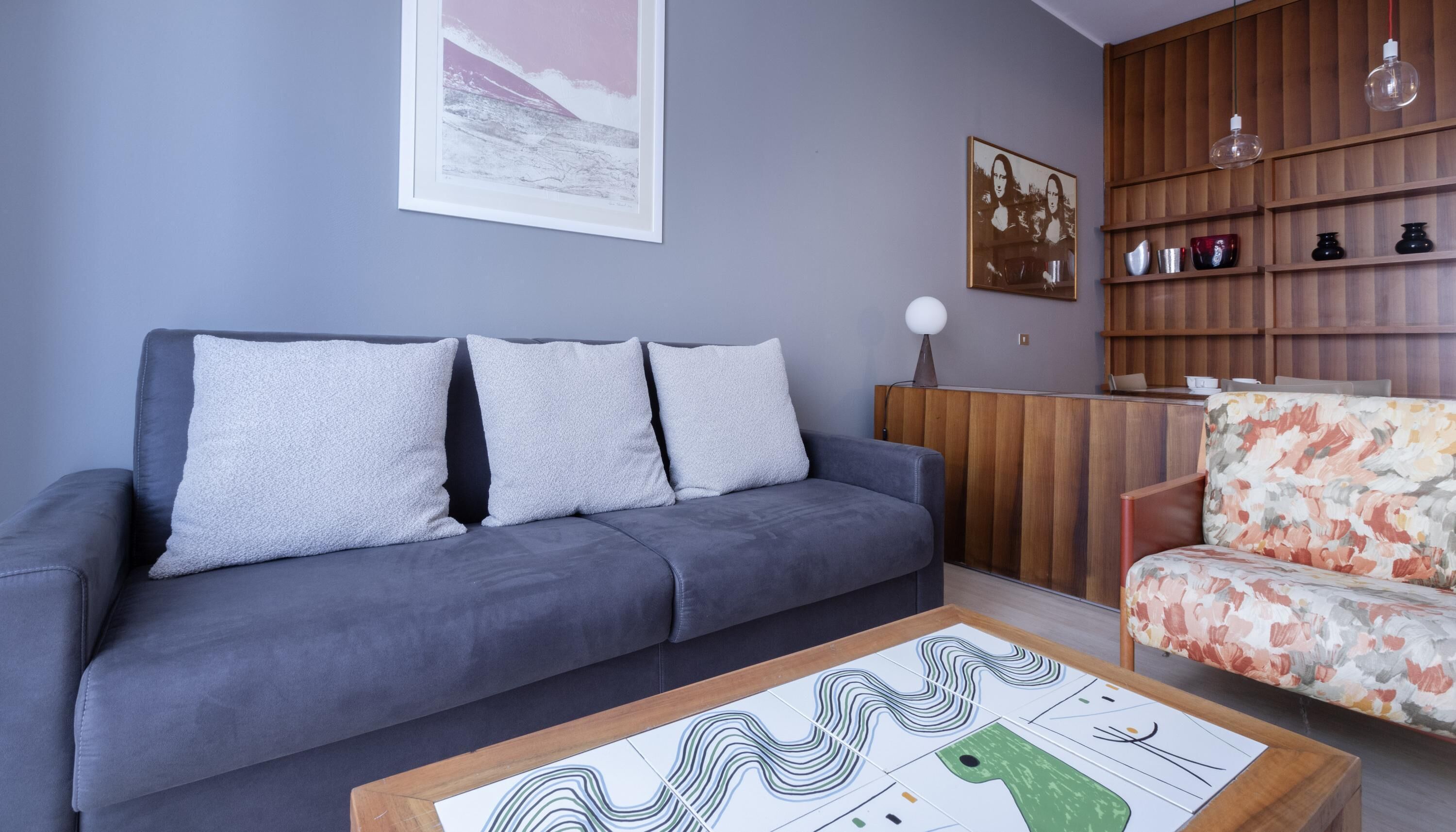 A modern living room with a grey sofa, a floral armchair, and a coffee table with abstract art.