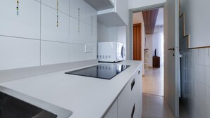 Una cocina moderna con muebles blancos, una placa de inducción negra y un microondas blanco.