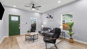 A modern living room with a green door, a ceiling fan, a sofa, a coffee table, and a potted plant. - Charming Walkable 4 BR 2 5 BA Near Dtown Riverwalk (San Antonio)