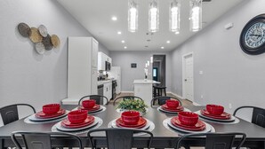 A dining area with a long table set for six, surrounded by black chairs. There are red bowls and plates on the table, and a potted plant in the center. The room has white walls and a ceiling with recessed lighting. - Charming Walkable 4 BR 2 5 BA Near Dtown Riverwalk (San Antonio)