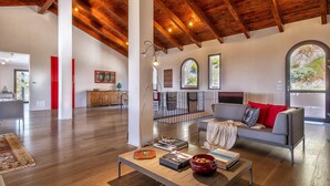 A spacious living area with a wooden ceiling, a grey sofa with red cushions, a coffee table with books and a bowl, and a view through an arched window. - Sardinia Re - Villa Posta Del Sol (Alghero)