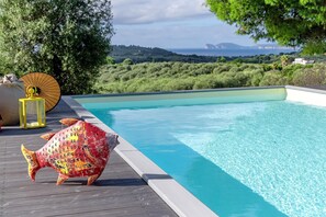 A swimming pool with a wooden deck, a large decorative fish sculpture, and a view of a coastal landscape. - Sardinia Re - Villa Posta Del Sol (Alghero)