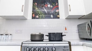 A kitchen with white cabinets, a stove, and a microwave. There is a painting above the stove. - Stunning 1-bed Apartment in Birmingham (Birmingham)