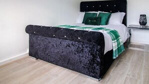 A bedroom with a black upholstered bed, a green and white bedspread, and a nightstand with a glass. - Stunning 1-bed Apartment in Birmingham (Birmingham)