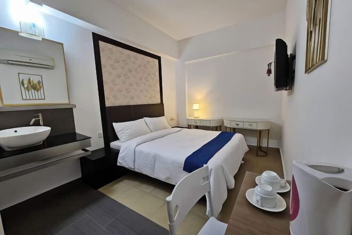 Une chambre d’hôtel avec un lit, une table de chevet, une télévision, un lavabo et un miroir.