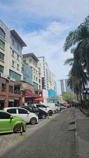 A street with parked cars and buildings, including a hotel and various shops. - Warisan Hotel (Kota Kinabalu)