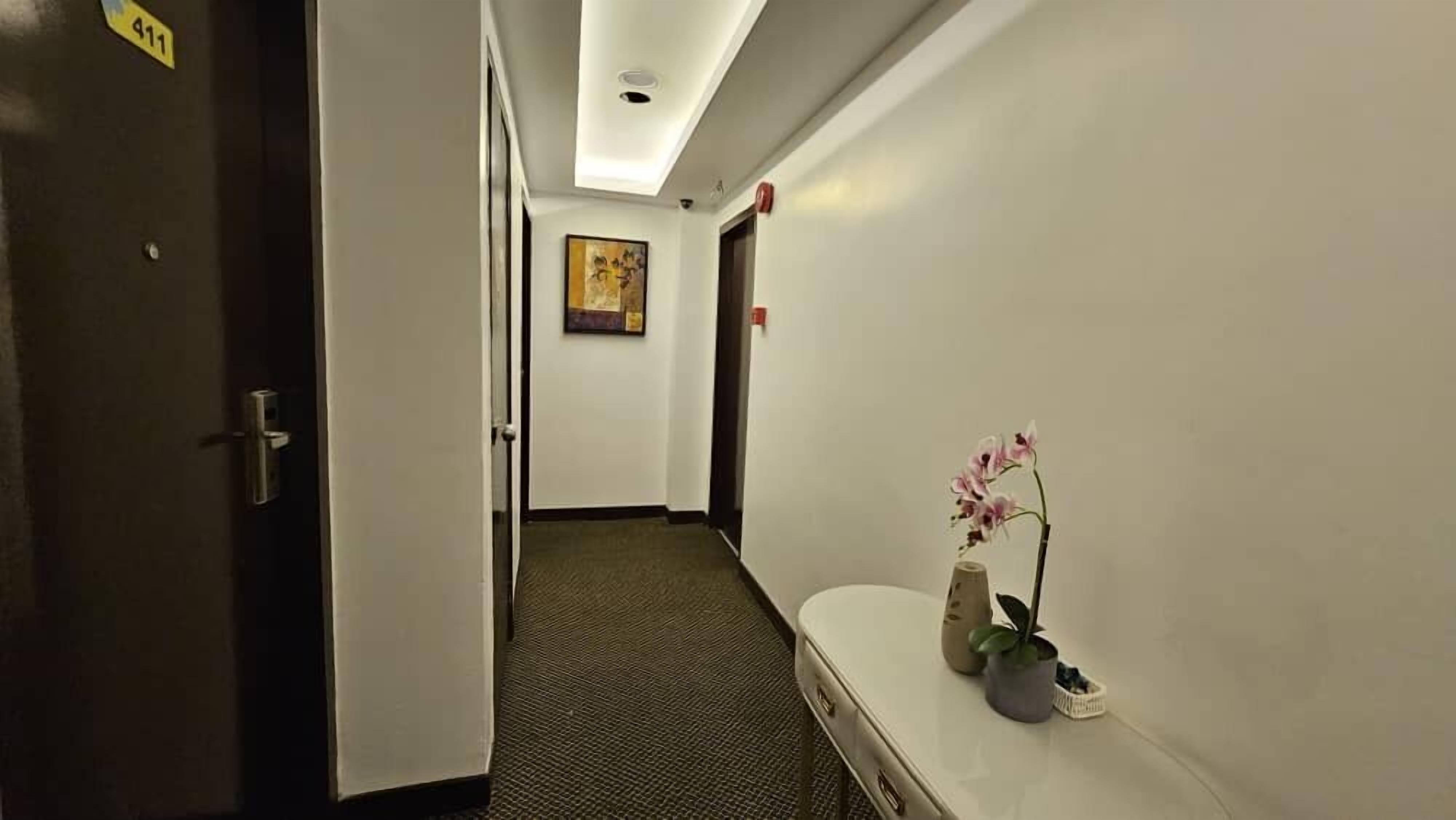 A hotel hallway with a carpeted floor, a painting on the wall, and a vase with flowers on a counter.