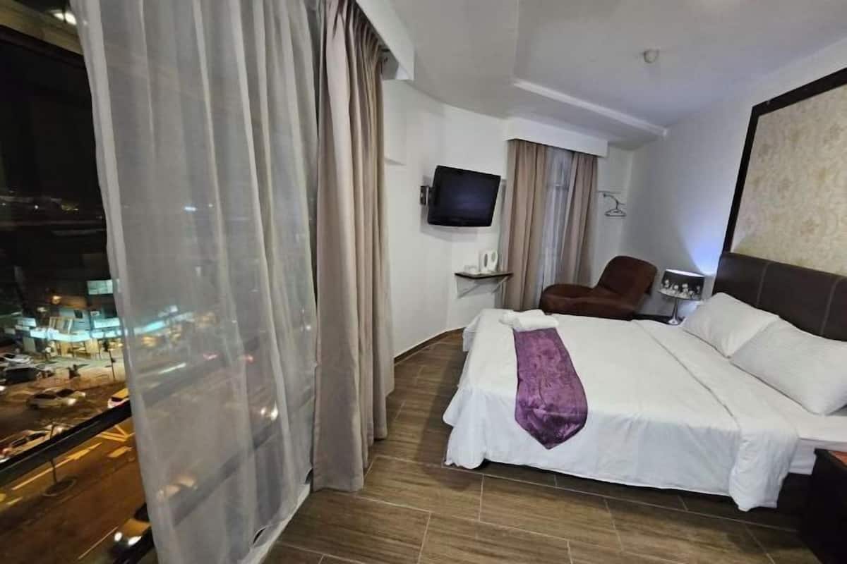 Une chambre d’hôtel avec un lit, une télévision, une chaise et une vue sur la ville par la fenêtre.