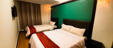 A hotel room with two beds, a green accent wall, and a wooden floor.