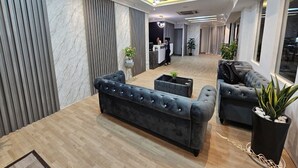 A modern hotel lobby with a reception desk, dark upholstered sofas, wooden flooring, and a ceiling with recessed lighting. - Warisan Hotel (Kota Kinabalu)