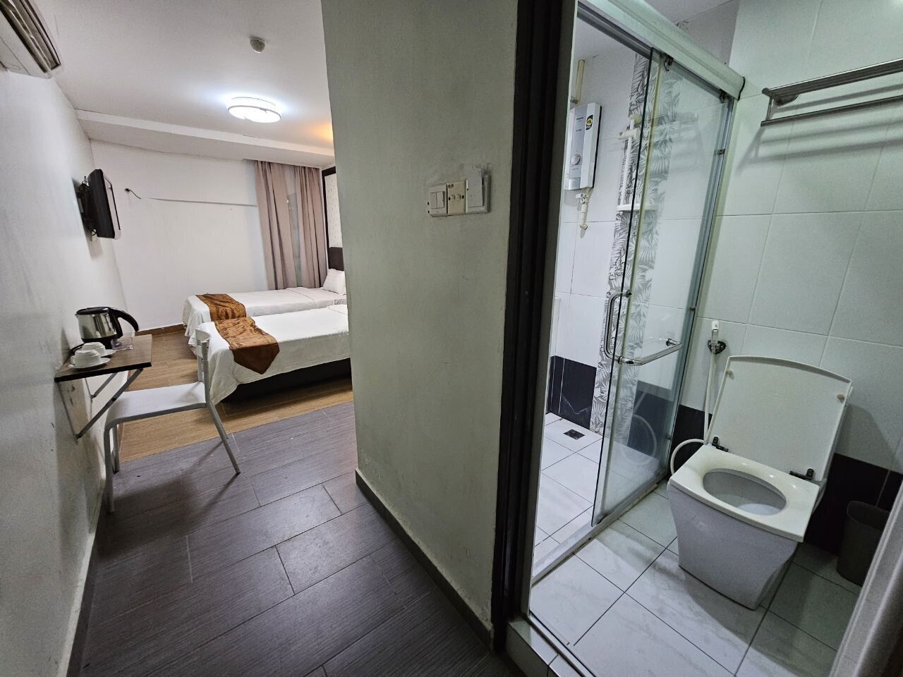 A hotel room with a bed, a small table with a kettle, a shower area, and a toilet.