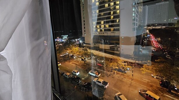 A nighttime cityscape through a window with reflections of buildings and traffic. - Warisan Hotel (Kota Kinabalu)