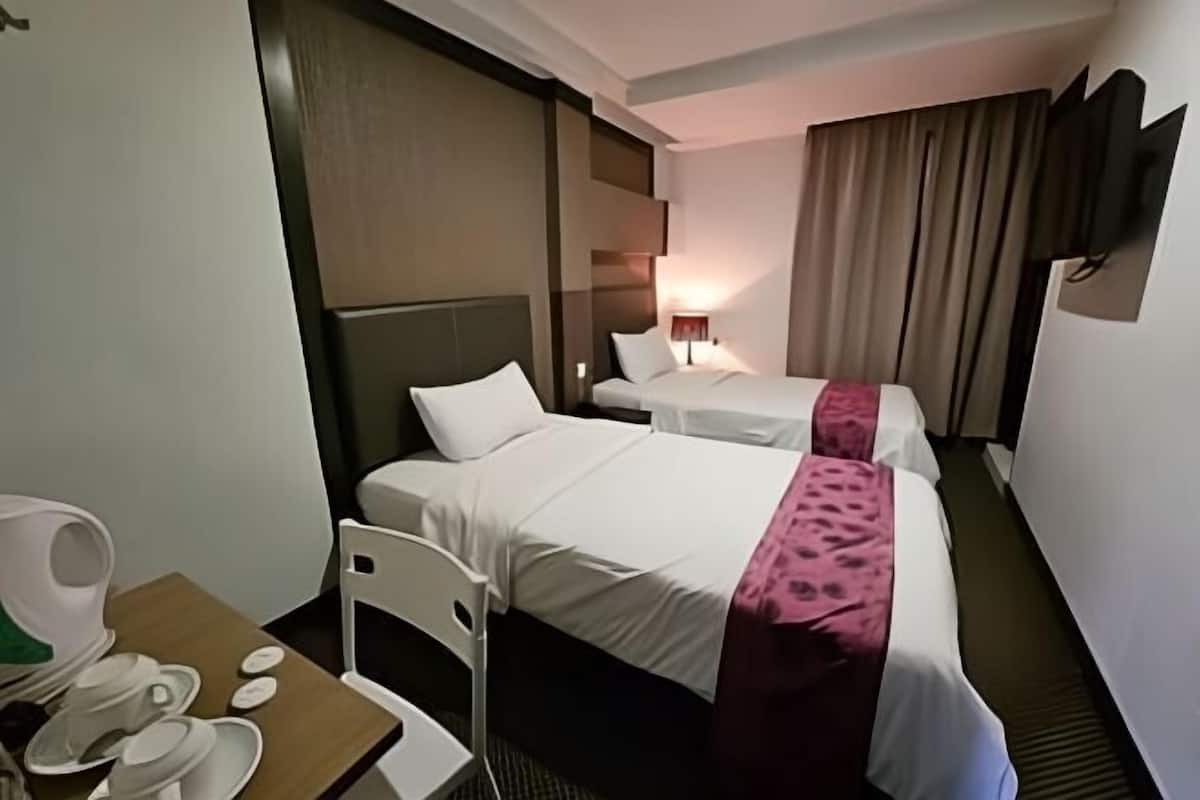Une chambre d’hôtel avec deux lits, un bureau avec une chaise, une télévision et une lampe.