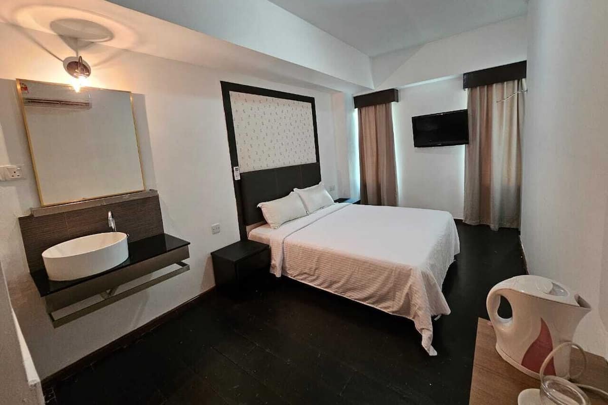 Une chambre d’hôtel comprenant un lit, une table de chevet, un lavabo intégré, un miroir, une télévision et un luminaire au plafond.
