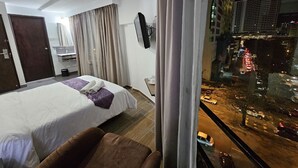A hotel room with a bed, a sofa, a TV, and a window with a city view. - Warisan Hotel (Kota Kinabalu)