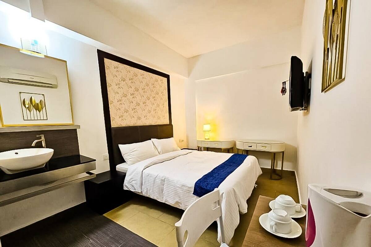 Une chambre d’hôtel avec un lit, des tables de chevet, une télévision, un lavabo et un miroir.