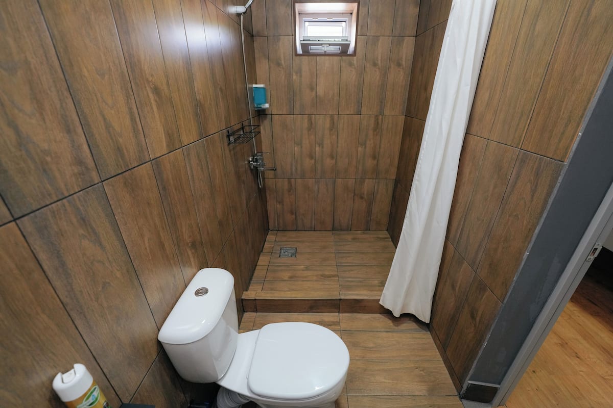 Un baño pequeño y compacto con paredes de madera, inodoro blanco, zona de ducha y un ventanal.