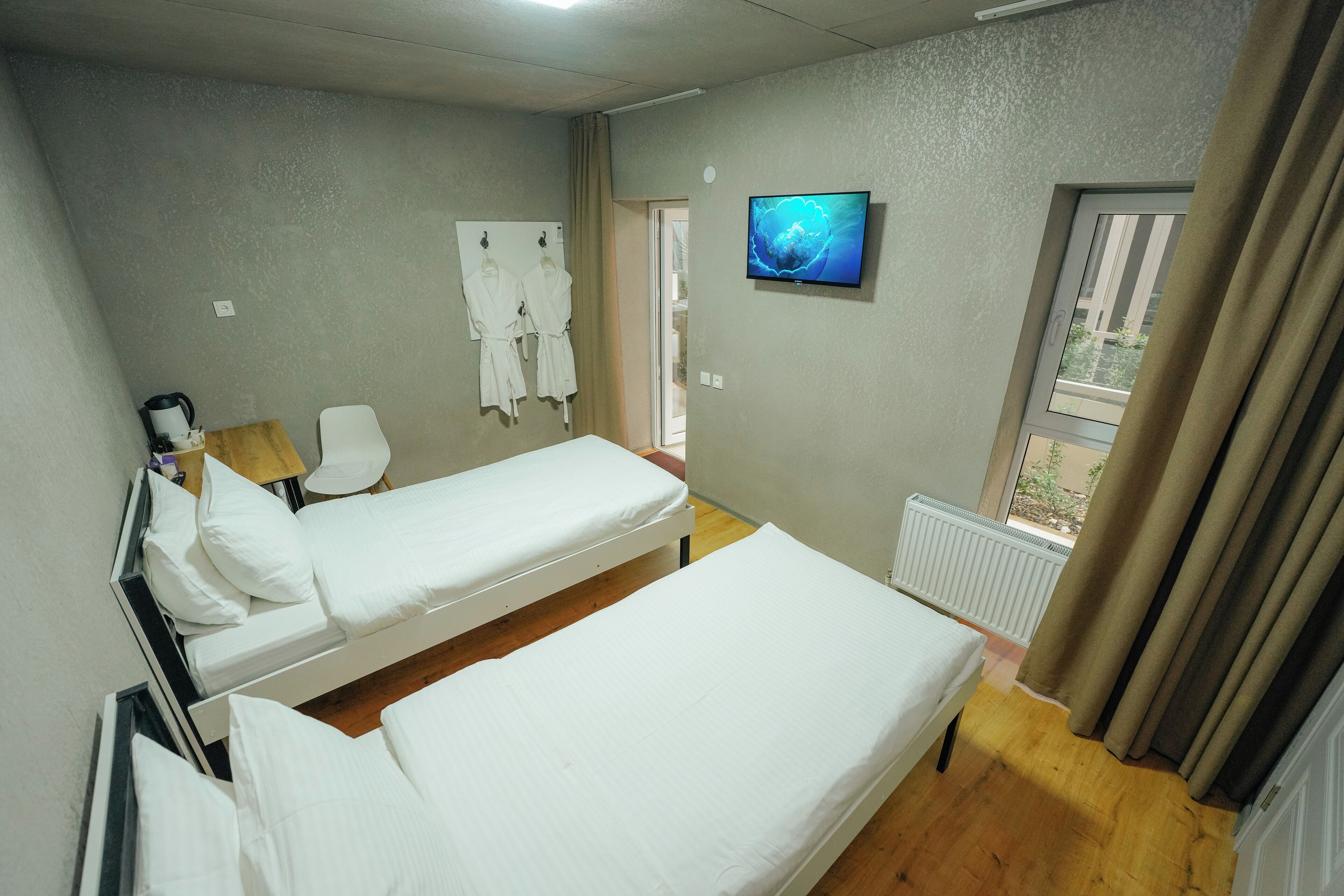 A hotel room with two single beds, a TV, a radiator, and a window with curtains.