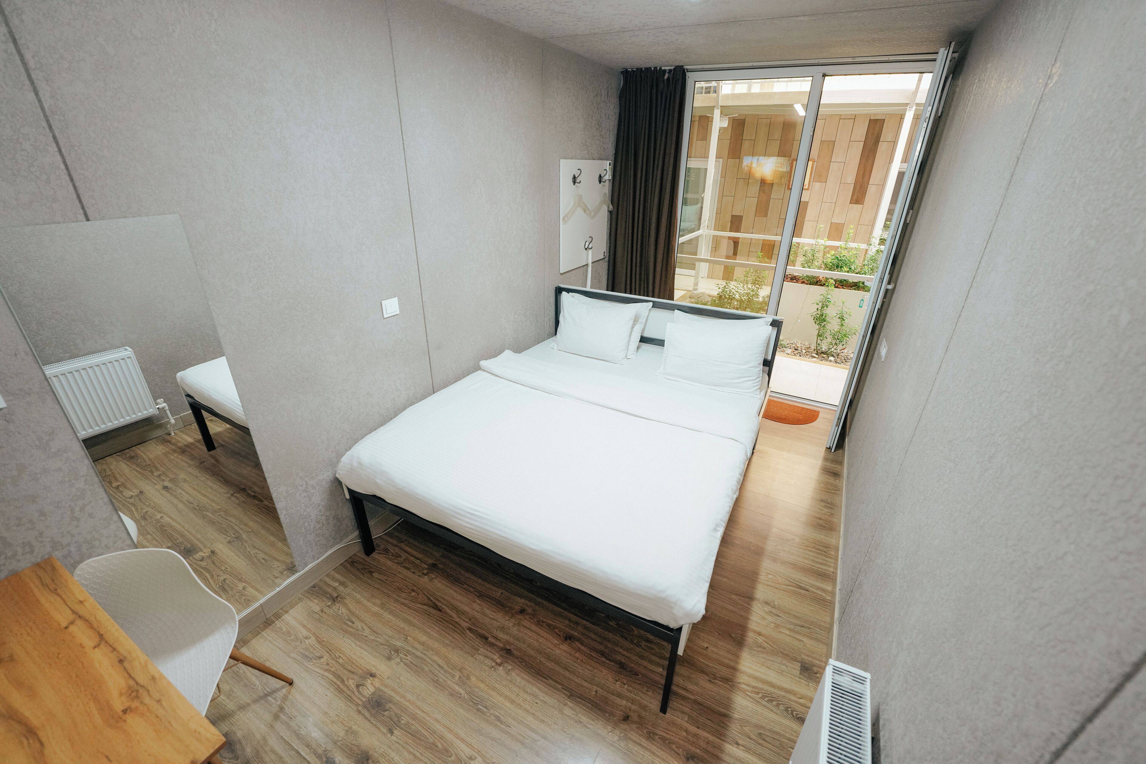 Una habitación de hotel moderna con una cama grande, una mesita de noche pequeña, un radiador y vistas al exterior.